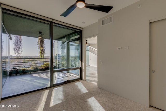 carpeted spare room featuring floor to ceiling windows, a ceiling fan, and visible vents