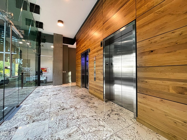 hallway with elevator, wooden walls, and marble finish floor