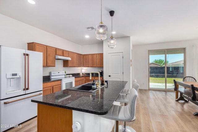 kitchen featuring brown cabinets, under cabinet range hood, visible vents, a sink, and white appliances