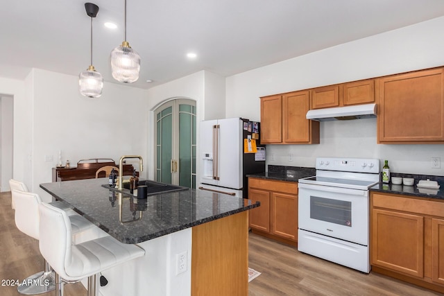 kitchen with brown cabinetry, a sink, under cabinet range hood, and white appliances