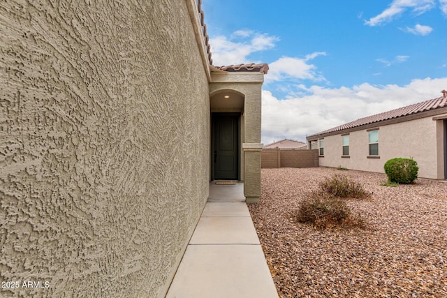 view of property exterior featuring a tile roof, stucco siding, and fence