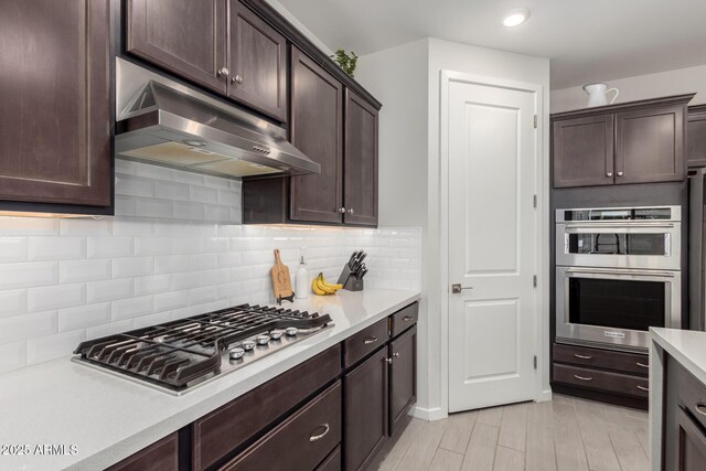 17311 W Seldon Ln, Waddell, AZ 85355 - kitchen featuring under cabinet range hood, stainless steel appliances, dark brown cabinets, light countertops, and tasteful backsplash