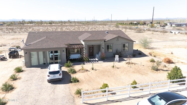 view of front of home featuring view of desert, a fenced front yard, a shingled roof, driveway, and stucco siding