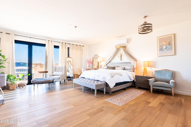 bedroom with baseboards, access to outside, an AC wall unit, and light wood-style floors