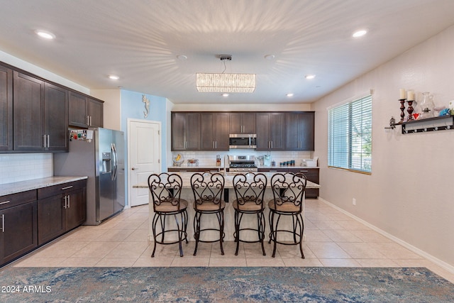 kitchen featuring backsplash, stainless steel appliances, dark brown cabinetry, light tile patterned floors, and a center island with sink