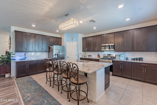 kitchen with visible vents, dark brown cabinets, a kitchen bar, tasteful backsplash, and stainless steel appliances