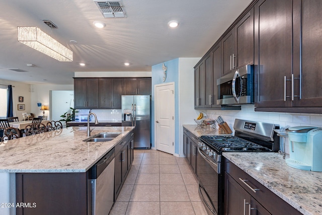 kitchen with dark brown cabinets, light stone countertops, appliances with stainless steel finishes, a sink, and backsplash