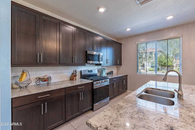 kitchen featuring decorative backsplash, light stone countertops, dark brown cabinets, a sink, and stainless steel appliances