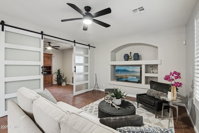 living room with a barn door, dark wood-type flooring, ceiling fan, and built in shelves