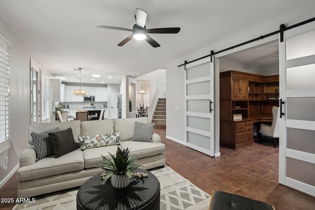 living room with a barn door, ceiling fan with notable chandelier, and dark tile patterned floors