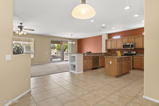 kitchen with pendant lighting, light colored carpet, ceiling fan with notable chandelier, appliances with stainless steel finishes, and a center island