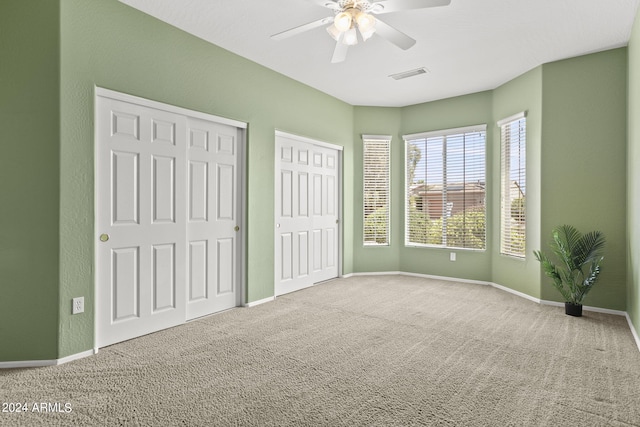 unfurnished bedroom with carpet, multiple closets, and ceiling fan