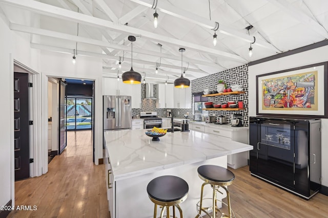 kitchen featuring appliances with stainless steel finishes, white cabinets, decorative backsplash, a kitchen island with sink, and light wood-style floors