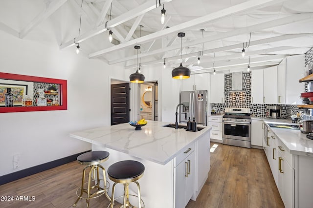 kitchen featuring appliances with stainless steel finishes, a sink, backsplash, wood finished floors, and white cabinetry