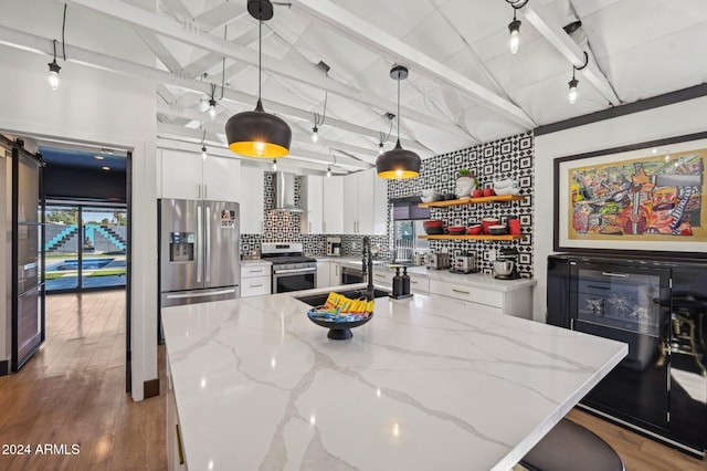 kitchen featuring stainless steel appliances, wall chimney range hood, white cabinetry, decorative backsplash, and a barn door
