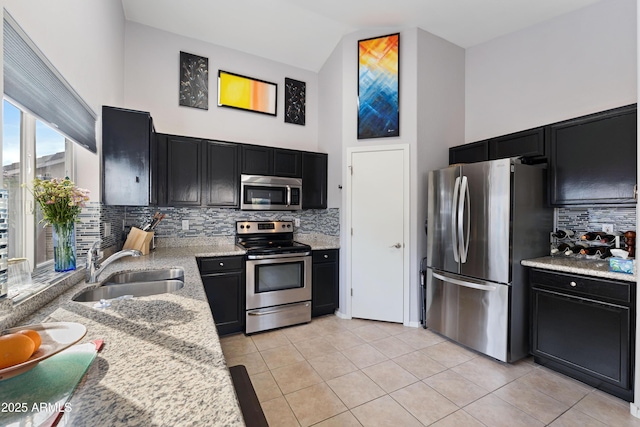 kitchen with sink, appliances with stainless steel finishes, high vaulted ceiling, light stone counters, and light tile patterned flooring