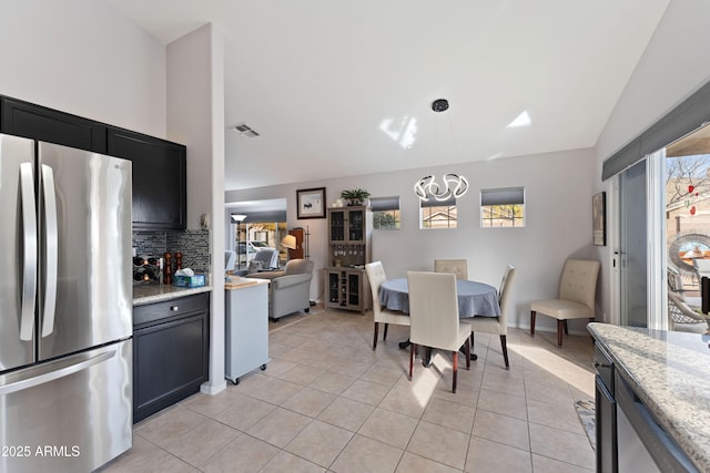 kitchen featuring light stone counters, lofted ceiling, stainless steel fridge, and hanging light fixtures