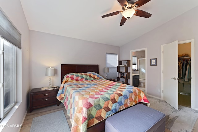 bedroom featuring light hardwood / wood-style flooring, ceiling fan, vaulted ceiling, ensuite bathroom, and a walk in closet