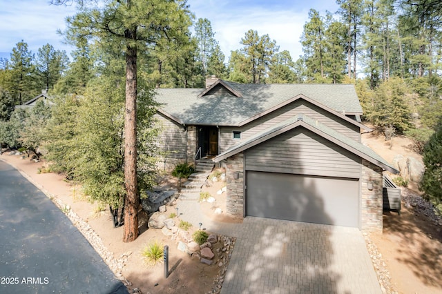 view of front of house with decorative driveway, a chimney, a shingled roof, a garage, and stone siding