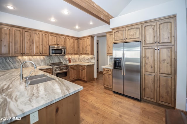 kitchen featuring a sink, appliances with stainless steel finishes, backsplash, light stone countertops, and light wood finished floors