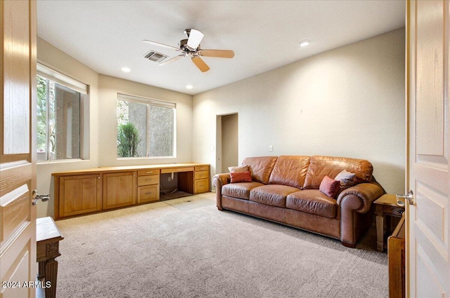 living room with light carpet, built in desk, and ceiling fan