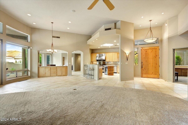 unfurnished living room with ceiling fan with notable chandelier, a towering ceiling, and light colored carpet