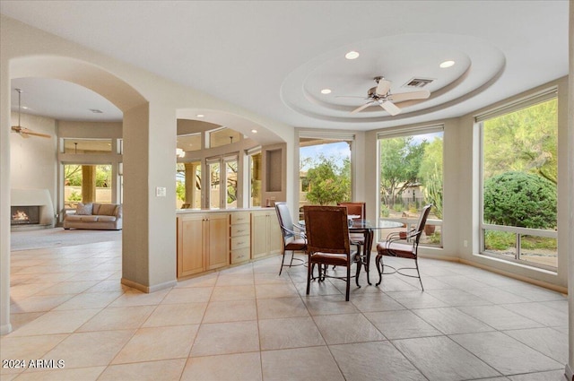 tiled dining room with ceiling fan, a tray ceiling, and plenty of natural light