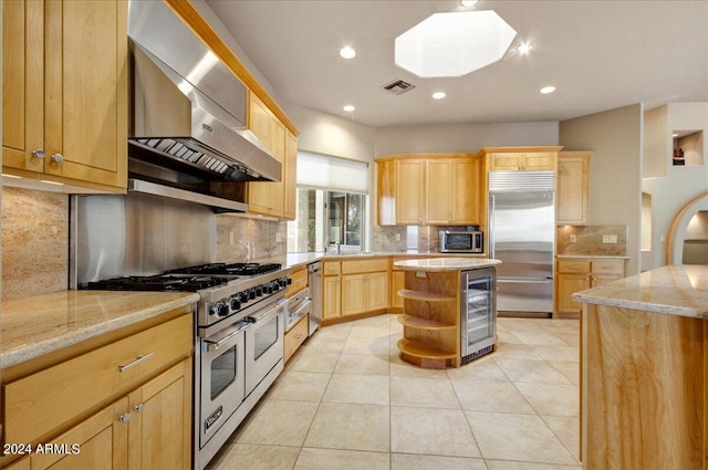 kitchen with light stone countertops, a center island, high end appliances, wall chimney exhaust hood, and beverage cooler