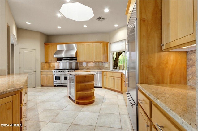 kitchen featuring appliances with stainless steel finishes, wall chimney exhaust hood, light brown cabinets, and tasteful backsplash