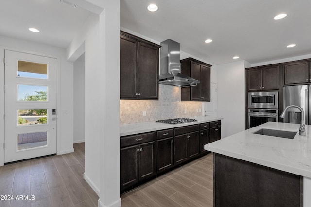 kitchen featuring tasteful backsplash, appliances with stainless steel finishes, light hardwood / wood-style floors, wall chimney exhaust hood, and sink