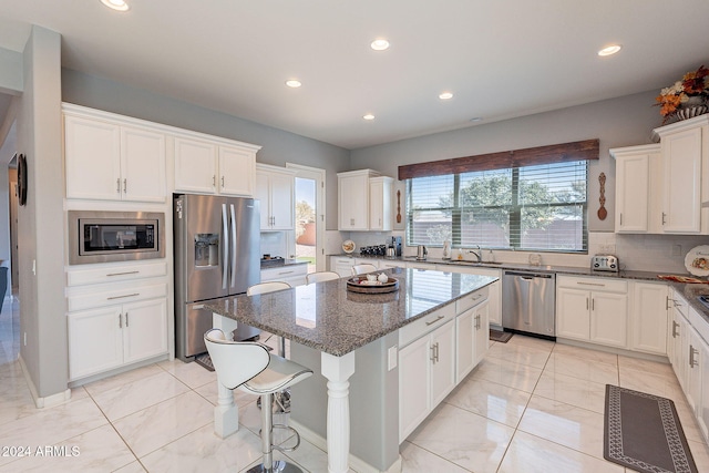 kitchen with a center island, white cabinets, decorative backsplash, dark stone countertops, and stainless steel appliances