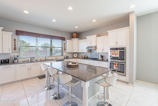 kitchen featuring a kitchen bar, dark stone counters, stainless steel appliances, sink, and a kitchen island