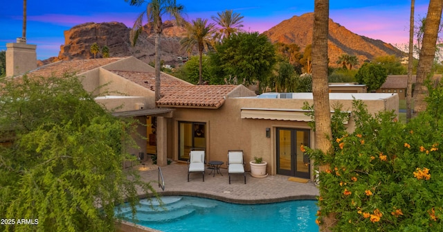 4450 E Camelback Rd Unit 4, Phoenix, AZ 85018 - back of house at dusk featuring french doors, an outdoor pool, a patio area, a mountain view, and stucco siding
