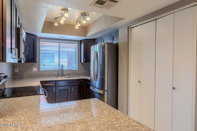 kitchen with sink, stainless steel appliances, light stone counters, a textured ceiling, and a raised ceiling