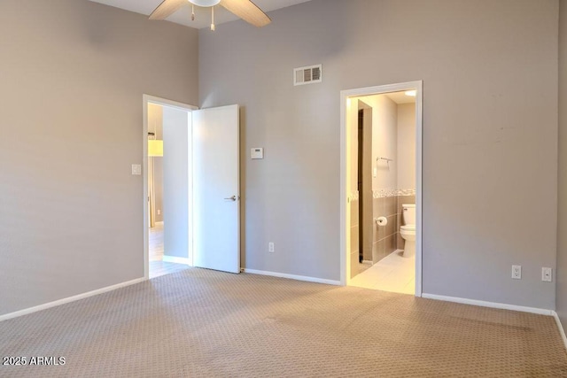 unfurnished bedroom featuring light carpet, ensuite bath, ceiling fan, and a high ceiling