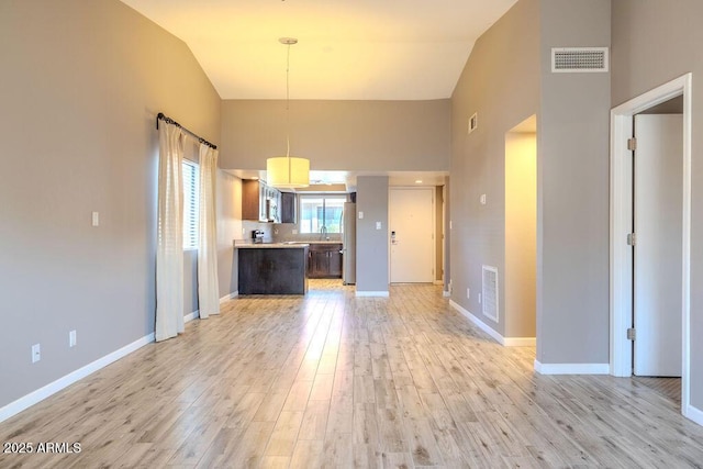 kitchen with pendant lighting, high vaulted ceiling, light hardwood / wood-style floors, and stainless steel refrigerator