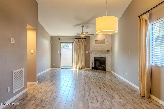 unfurnished living room featuring a stone fireplace, light wood-type flooring, and a wealth of natural light