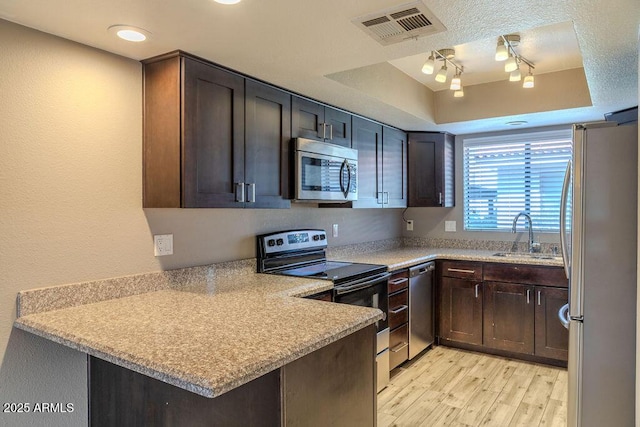 kitchen with sink, appliances with stainless steel finishes, light hardwood / wood-style floors, kitchen peninsula, and a raised ceiling