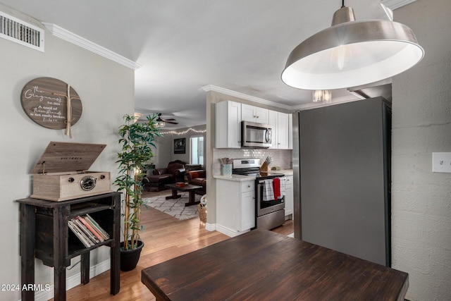 kitchen with white cabinets, crown molding, appliances with stainless steel finishes, tasteful backsplash, and light hardwood / wood-style floors