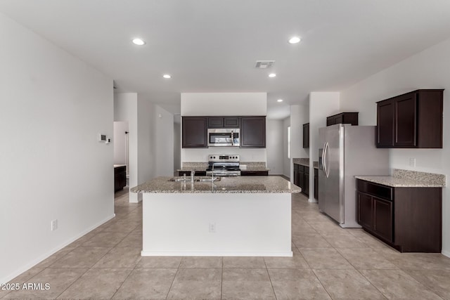 28259 N Chalcocite St, San Tan Valley, AZ 85143 - kitchen featuring appliances with stainless steel finishes, a kitchen island with sink, dark brown cabinetry, light stone counters, and recessed lighting