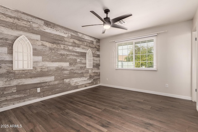 empty room featuring a ceiling fan, dark wood-style flooring, visible vents, wooden walls, and an accent wall