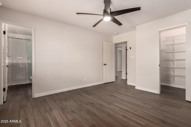 unfurnished bedroom with baseboards, ensuite bathroom, ceiling fan, dark wood-type flooring, and a spacious closet