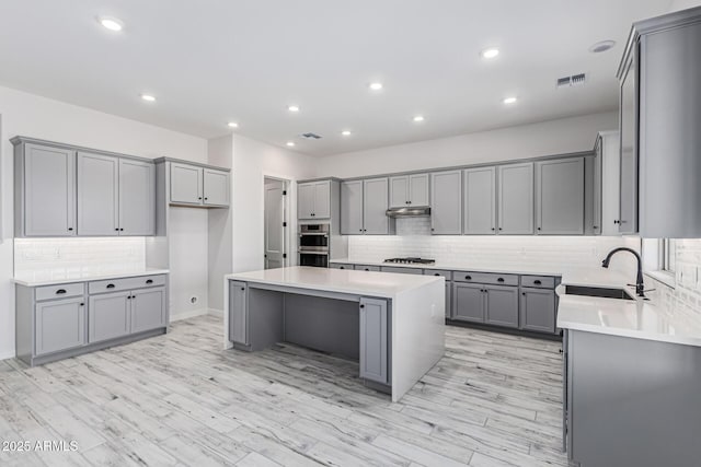 17322 W Puget Ave, Waddell, AZ 85355 - kitchen featuring gray cabinets, a center island, decorative backsplash, under cabinet range hood, and light countertops