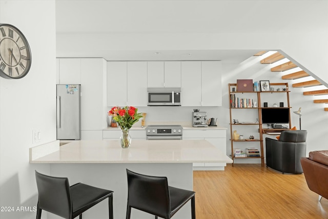 kitchen with stainless steel appliances, light hardwood / wood-style floors, white cabinets, a kitchen bar, and kitchen peninsula