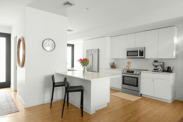 kitchen with a breakfast bar, white cabinetry, kitchen peninsula, stainless steel appliances, and light hardwood / wood-style flooring