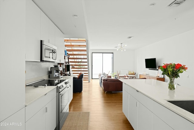 kitchen featuring stainless steel appliances, white cabinetry, an inviting chandelier, and light wood-type flooring