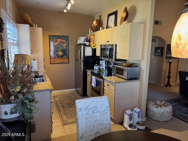 kitchen featuring track lighting, white cabinetry, stainless steel appliances, light tile patterned flooring, and light stone counters