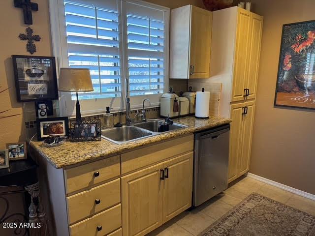 kitchen with stainless steel dishwasher, sink, light stone countertops, light brown cabinets, and light tile patterned floors