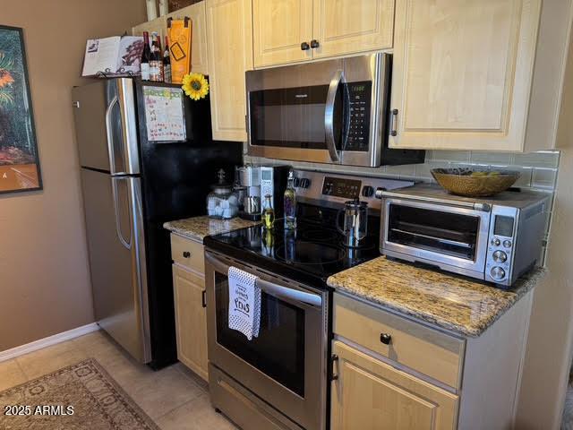 kitchen with light tile patterned floors, light stone countertops, light brown cabinets, and stainless steel appliances