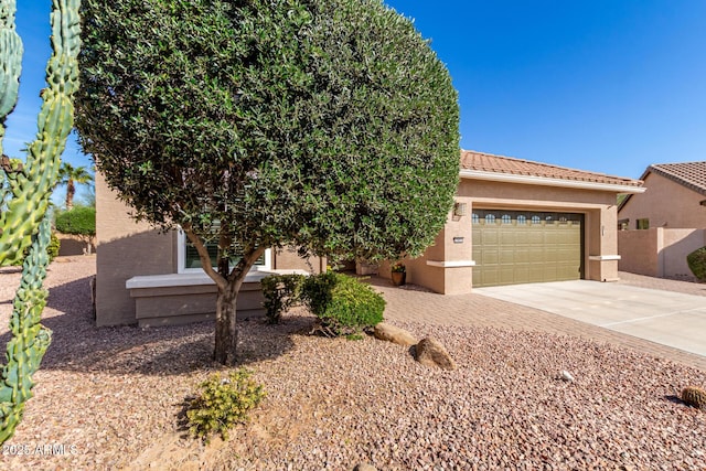 view of front of property featuring a garage, a tile roof, concrete driveway, and stucco siding